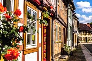 Uma fileira de edifícios europeus tradicionais, com porta e janelas vermelhas, rua de paralelepípedos e céu claro.