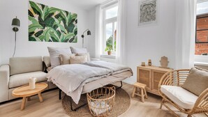A modern bedroom with a bed, a sofa, a wicker chair, and a small wooden table. - REGIOHOTEL am Nicolaiplatz Wernigerode (Wernigerode)