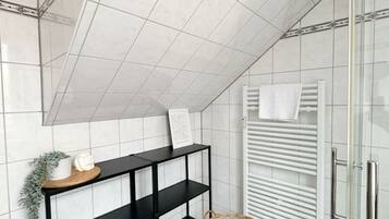 A bathroom with white tiled walls, a black shelf unit, a glass shower enclosure, and a white towel rack.