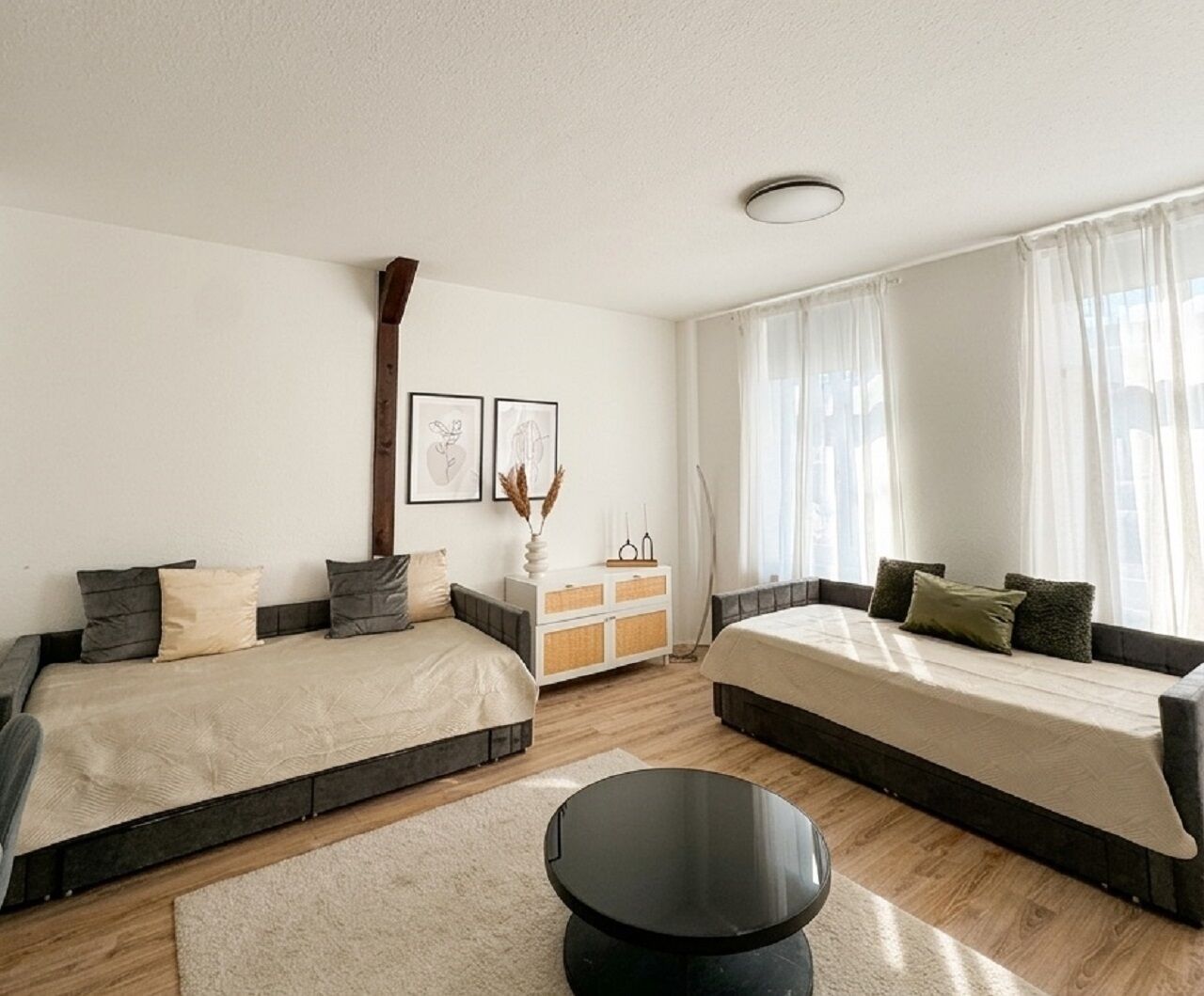 A modern bedroom with two beds, a round black table, and a white dresser.