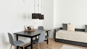 Una sala de estar moderna con una mesa de comedor, sillas grises, un sofá gris con un plaid color beige y una lámpara colgante.