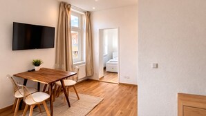 A modern room with a wooden table, chairs, a TV, and a window with curtains. - REGIOHOTEL am Nicolaiplatz Wernigerode (Wernigerode)