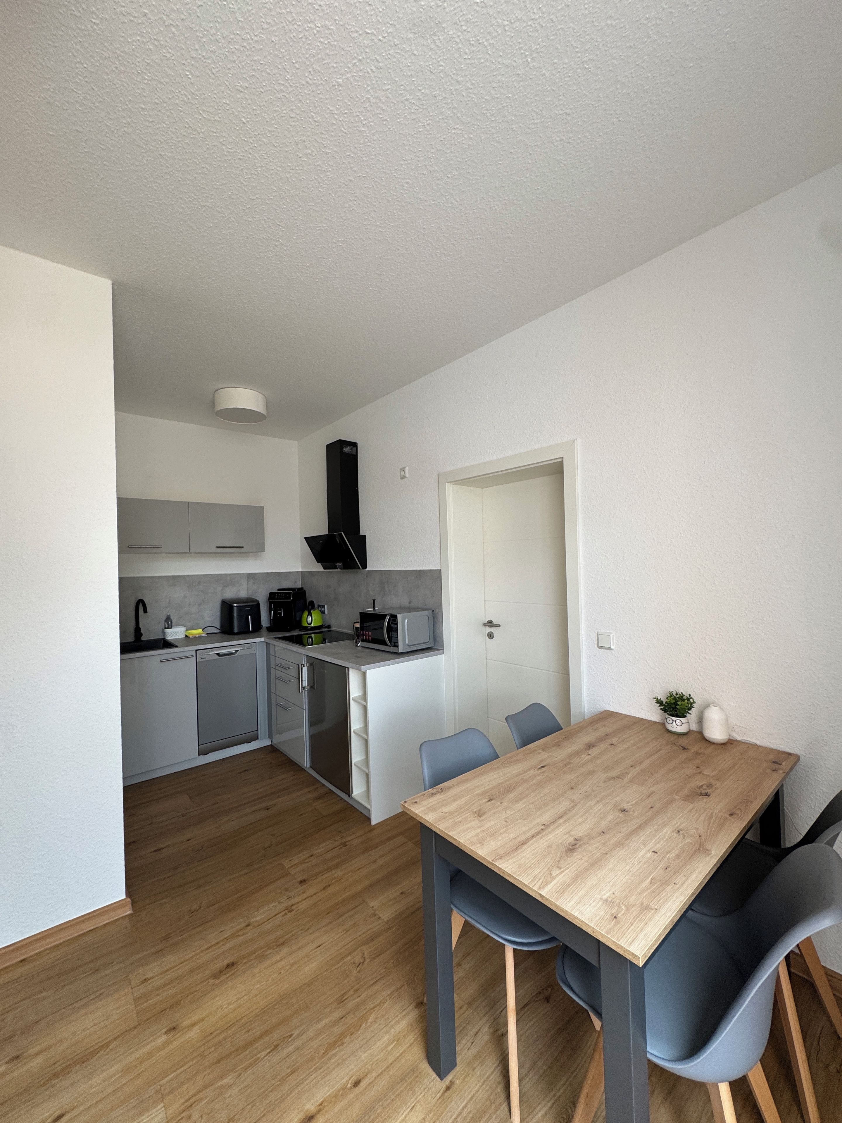 A modern kitchen with grey cabinets, a black range hood, and a dining area with a wooden table and blue chairs.