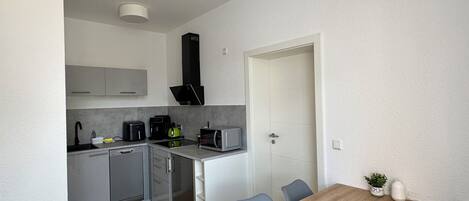 A modern kitchen with grey cabinets, a black range hood, and a dining area with a wooden table and blue chairs.