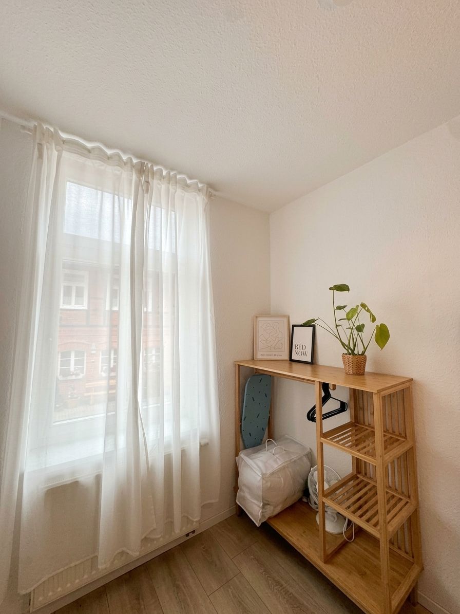 A room with a wooden shelf unit, a white cushion, a fan, and a potted plant.