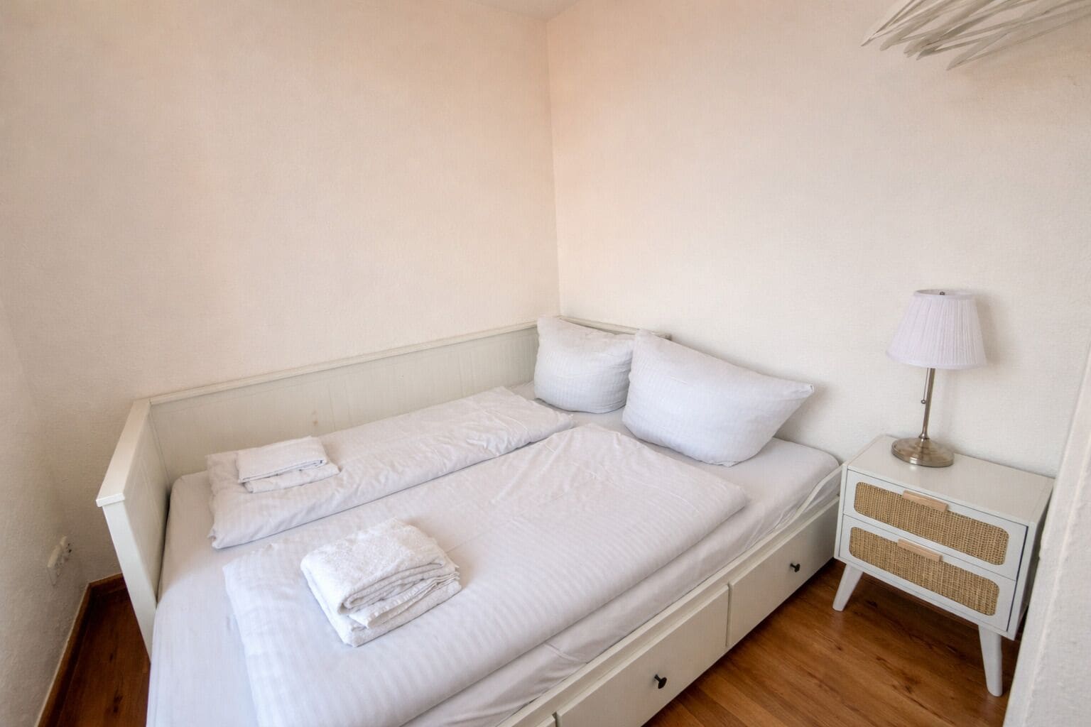 Un lit simple avec une literie blanche, une lampe de chevet et une petite table de chevet sur laquelle se trouve un panier en osier.
