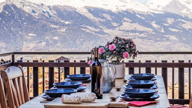 A table set with plates and a bottle, overlooking a snowy mountain range.