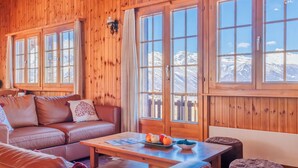 A cozy cabin interior with a wooden interior, a leather sofa, a coffee table with fruits, and large windows offering a mountain view.