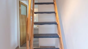 Un escalier en bois, dont les marches sont recouvertes d’une moquette bleue, mène à une porte.