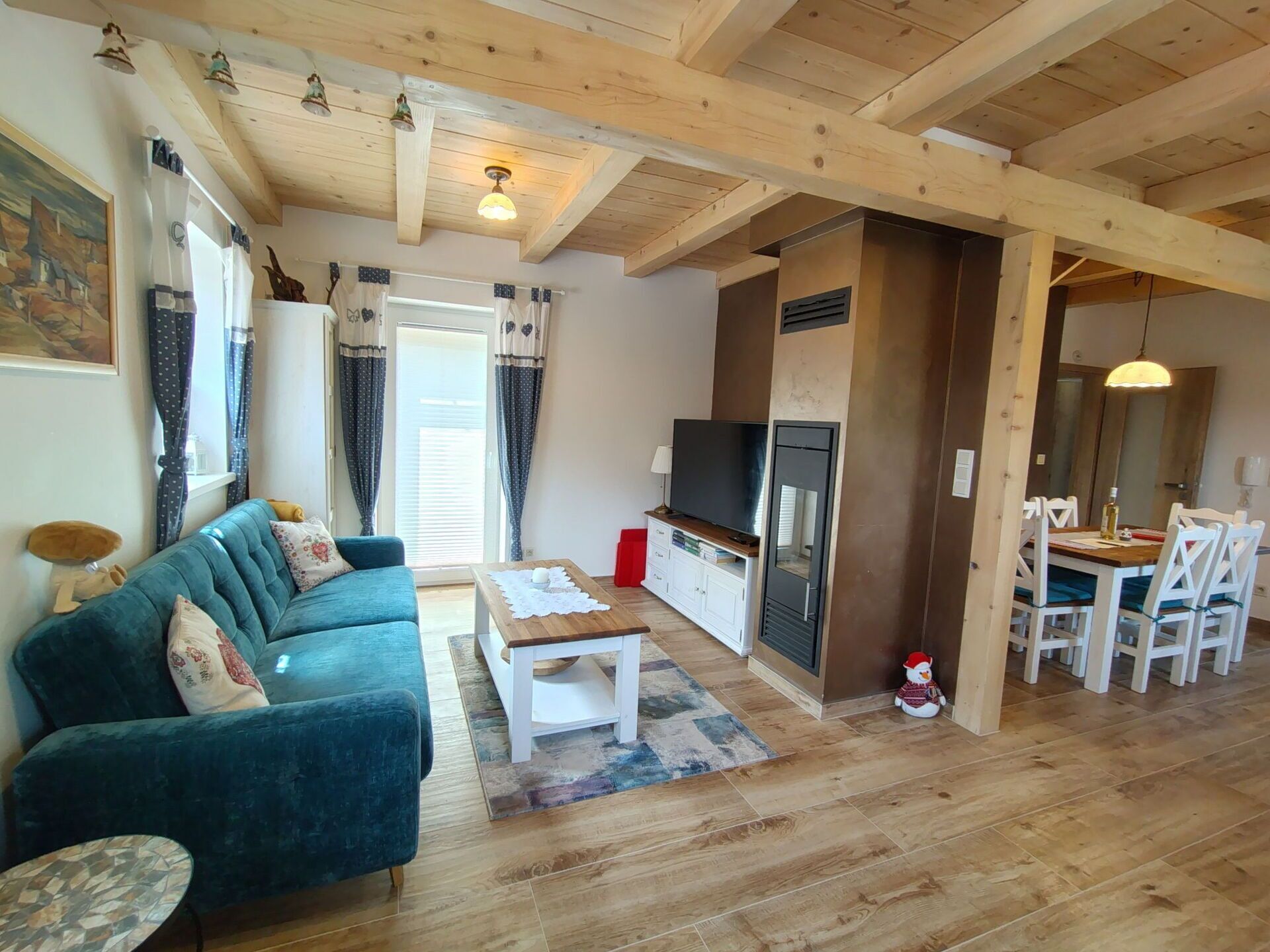 A cozy living room with a blue sofa, a wooden coffee table, and a TV. There's a dining area with a table and chairs, and a kitchen area with a stove and cabinets.