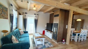 A cozy living room with a blue sofa, a wooden coffee table, and a TV. There's a dining area with a table and chairs, and a kitchen area with a stove and cabinets.