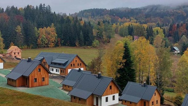 A cluster of wooden cabins with sloped roofs, surrounded by a forested landscape.