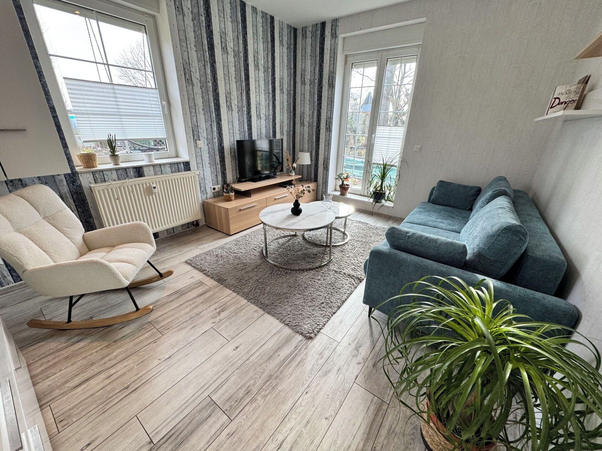 Een woonkamer met een bank, een fauteuil, een salontafel, een televisie en een potplant.