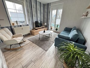 Una sala de estar con un sofá, una silla, una mesa de centro, un televisor y una planta en maceta.