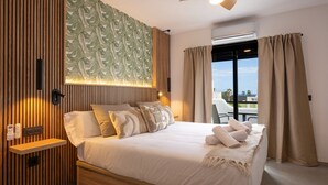 Ein modernes Hotelzimmer mit einem großen Bett, Holzvertäfelung, einer Wand mit grünem Blattmuster und einem Balkon mit Vorhängen.