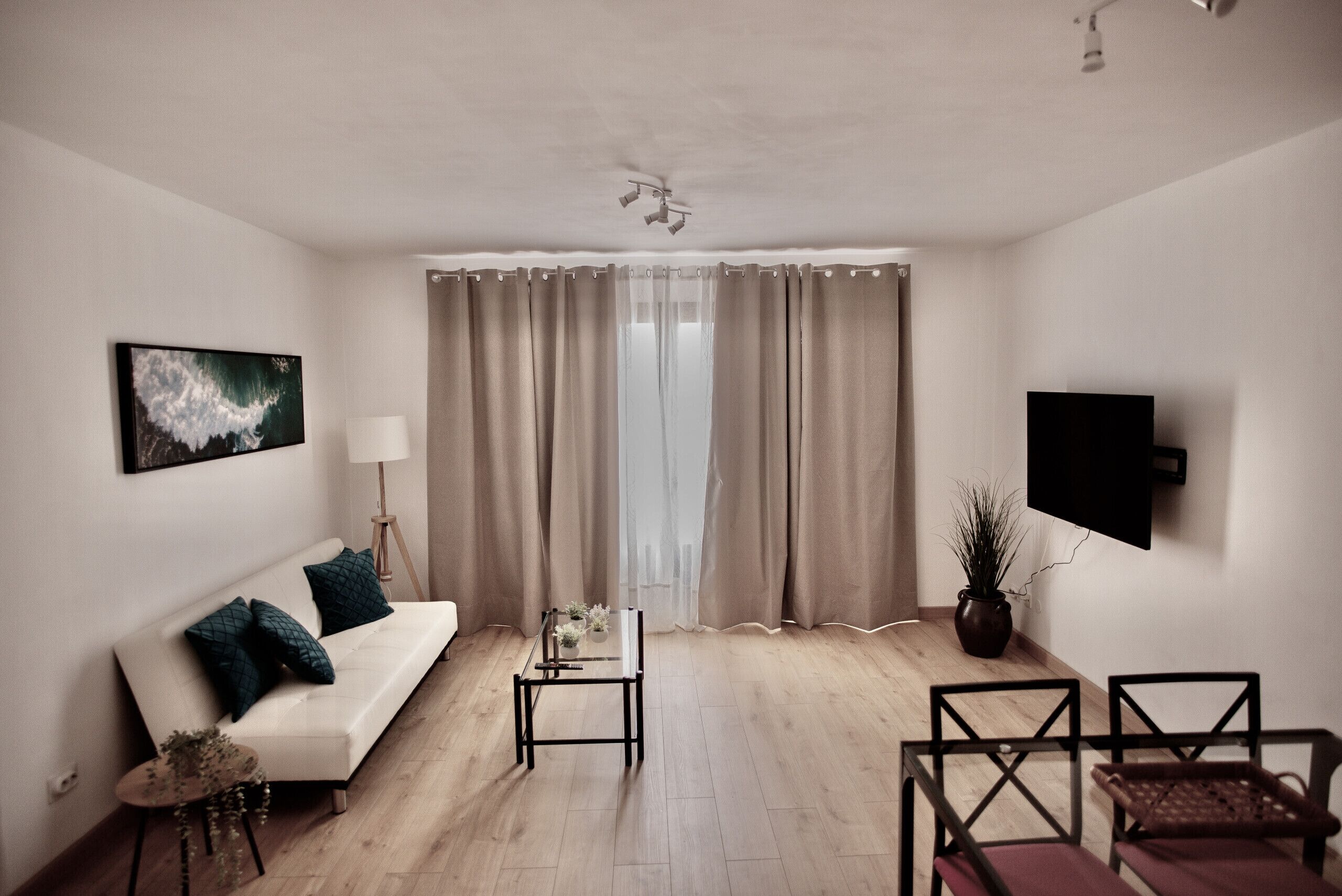 A modern living room with a white sofa, a glass coffee table, and a TV mounted on the wall.