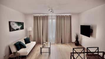 A modern living room with a white sofa, a glass coffee table, and a TV mounted on the wall.
