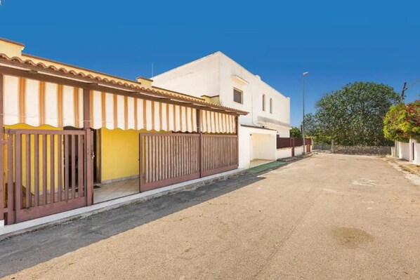 Una calle residencial con casas, un acceso con reja y un cielo despejado.