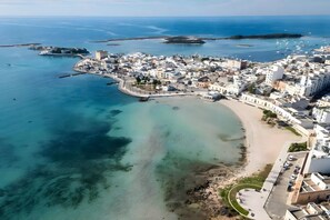 Vista aérea de un pueblo costero con playa, aguas cristalinas y edificios blancos.
