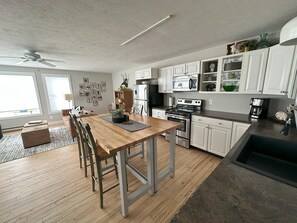 A modern kitchen with white cabinets, stainless steel appliances, and a wooden dining table.