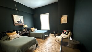 Una habitación con dos camas, una silla, una lámpara y una ventana.