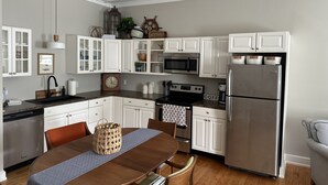 A modern kitchen with white cabinets, stainless steel appliances, and a wooden dining table.