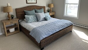 A bedroom with a large bed, two nightstands, a lamp, a framed picture, and a window.