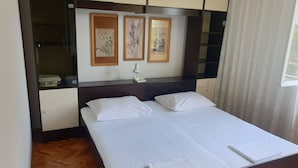Une chambre d’hôtel avec un lit, une table de chevet, une lampe et une armoire. Deux œuvres d’art encadrées sont accrochées au mur au-dessus du lit.