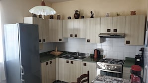 Une cuisine avec des meubles de couleur bois clair, un réfrigérateur en acier inoxydable, une cuisinière à gaz et une machine à café.
