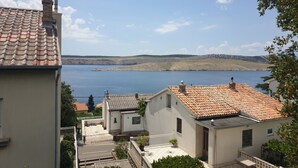 Un quartier résidentiel caractérisé par des toits recouverts de tuiles en terre cuite, une cour pavée et une vue sur une vaste étendue d’eau et des collines lointaines.
