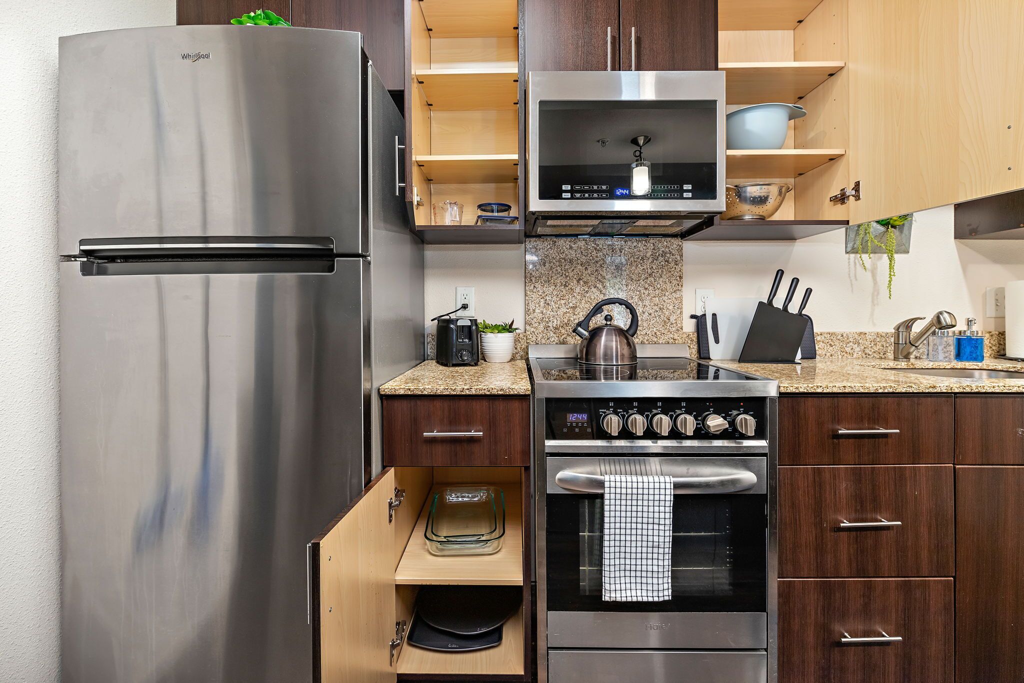 A modern kitchen with a stainless steel refrigerator, built-in microwave, oven, and a coffee maker.