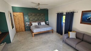 Un dormitorio con una cama, un armario de madera, una mesita de noche, un sofá gris y un ventilador de techo.