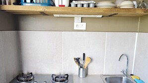 Una cocina compacta con estufa a gas, un fregadero y un taburete pequeño.