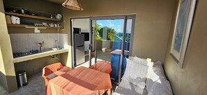 A compact kitchen with a sink, stove, and shelves, a dining area with a table and chairs, and a sliding glass door leading to an outdoor space.