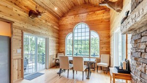 Interior de una cabaña de madera con una mesa de comedor, sillas y una chimenea de piedra.