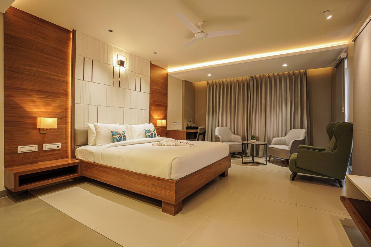 Quarto de hotel moderno com uma cama grande, uma escrivaninha, duas cadeiras e um ventilador de teto.
