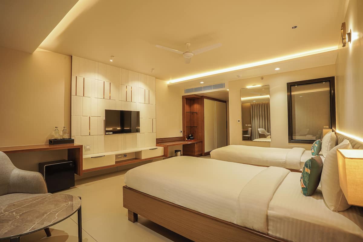 Quarto de hotel moderno com uma cama grande, escrivaninha, cadeira, televisão e espelho.