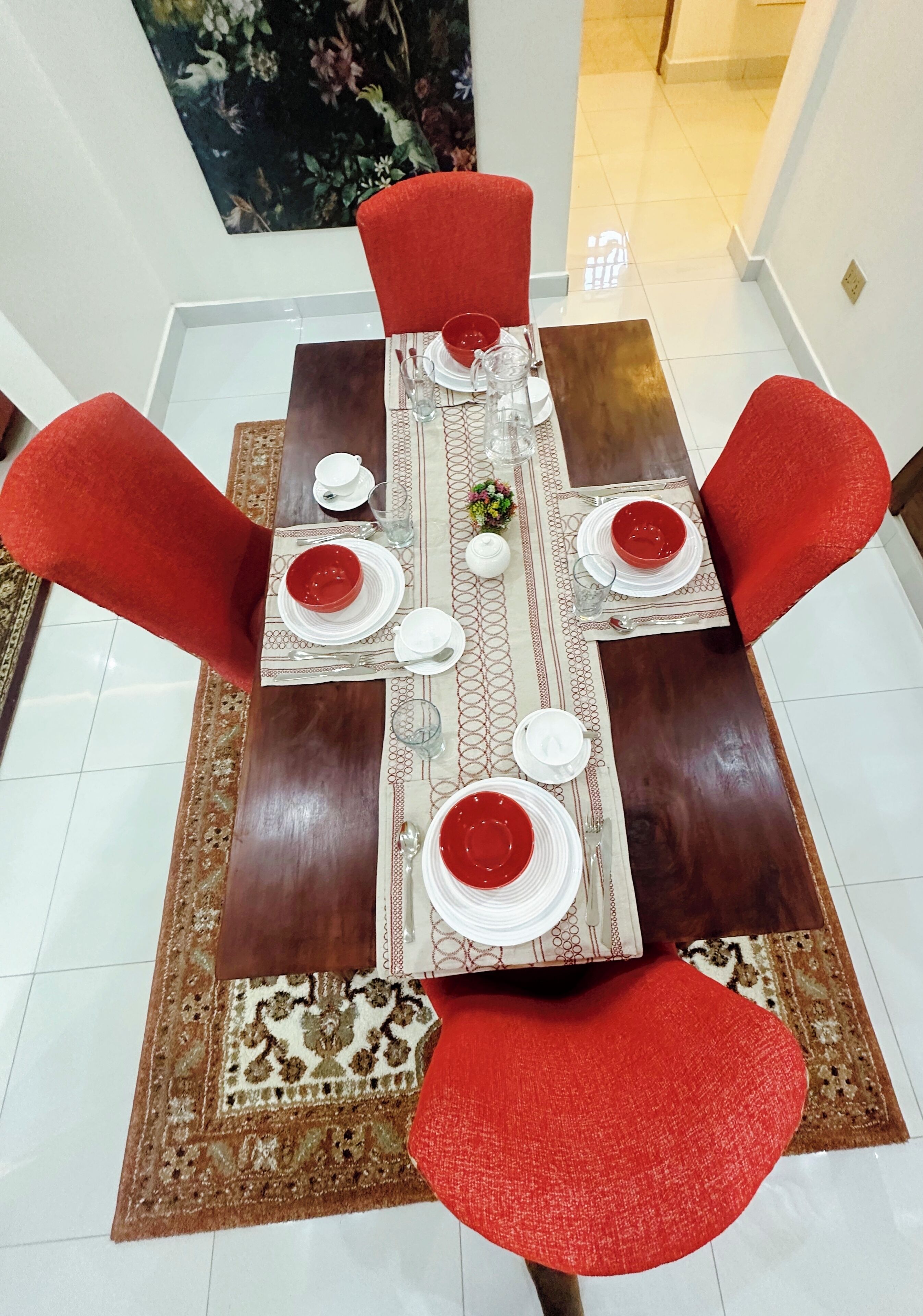 A dining table set with red chairs, white plates, and a patterned table runner.