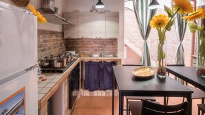 A kitchen with a brick wall, wooden ceiling, and hanging pendant lights. There is a dining table with a vase of sunflowers and a bowl. - Villetta Sogno Di Mare In Porto Cesareo (Porto Cesareo)
