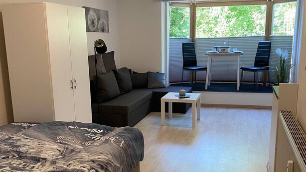 A modern, well-lit room with a bed, a sofa, a small table, and a dining area with chairs. - Vacation apartment "Twistesee" at the Edersee (Waldeck)