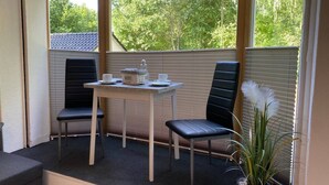 A covered patio area with a table and two chairs, a potted plant, and a view of trees through the window blinds. - Vacation apartment "Twistesee" at the Edersee (Waldeck)