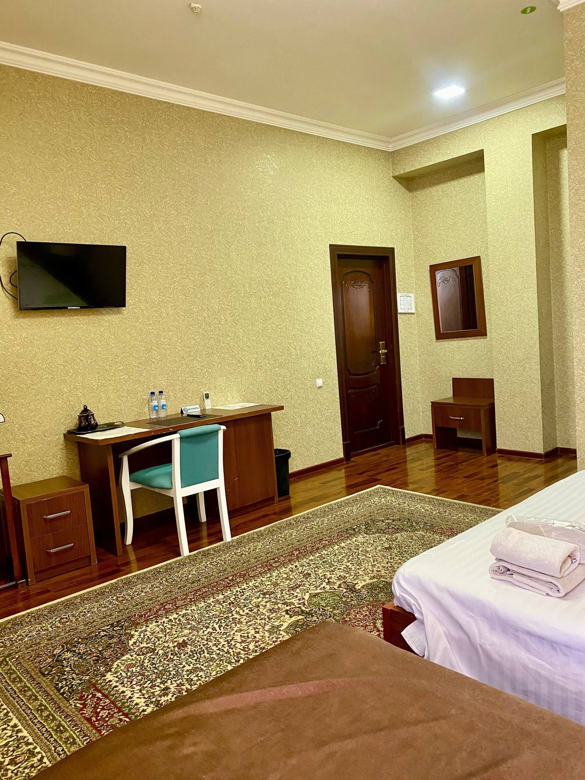 A hotel room with a bed, desk, chair, TV, and a door.