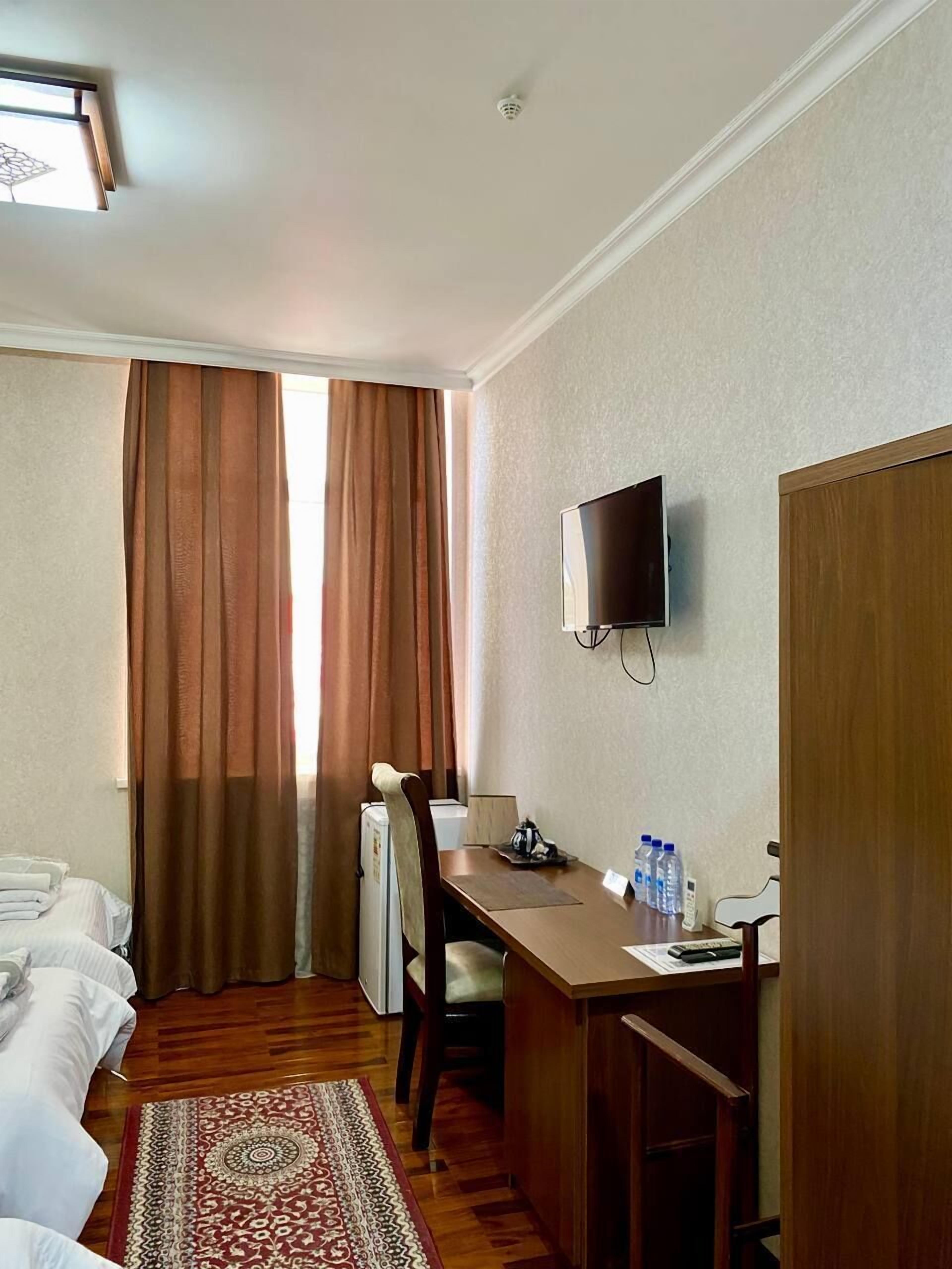 A hotel room with a bed, a desk, a chair, a television, and a window with curtains.