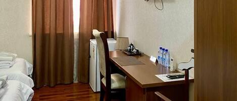 Habitación de hotel con cama, escritorio, silla, televisor y ventana con cortinas.
