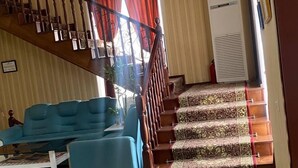 A living room with a blue sofa, a coffee table, a staircase with patterned carpet, and a wall-mounted air conditioner. - Vardonze  (Bukhara)