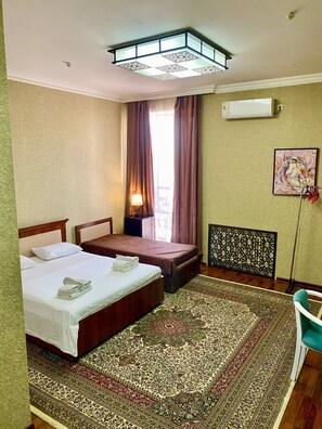 A hotel room with two beds, a large patterned rug, an air conditioning unit, and a window with curtains. - Vardonze  (Bukhara)