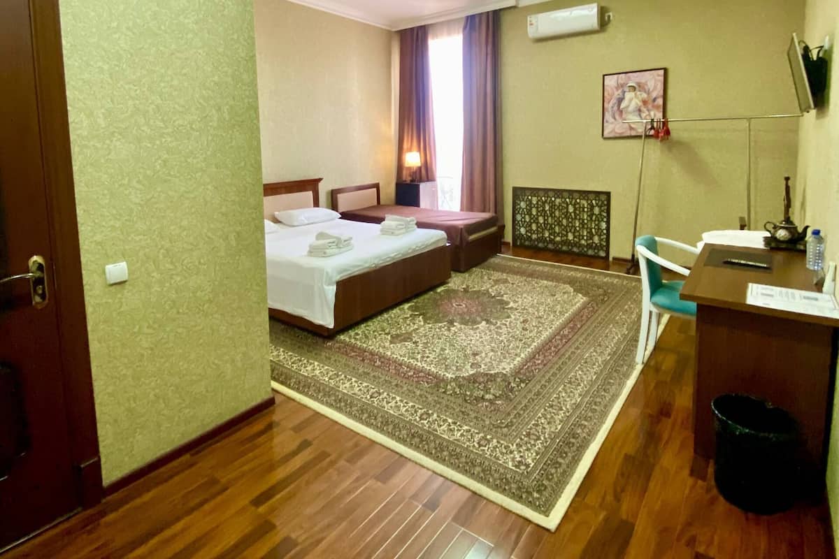 A hotel room with two beds, a desk, a chair, a rug, and an air conditioning unit.