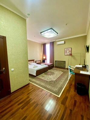 A hotel room with two beds, a desk, a chair, a rug, and an air conditioning unit. - Vardonze  (Bukhara)
