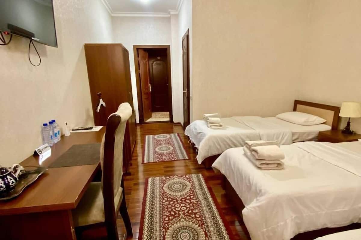 A hotel room with two single beds, a desk with a chair, a TV mounted on the wall, and a wooden floor.
