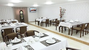 A hotel dining area with multiple tables set for dining, a clock on the wall, and a television screen. - Vardonze  (Bukhara)